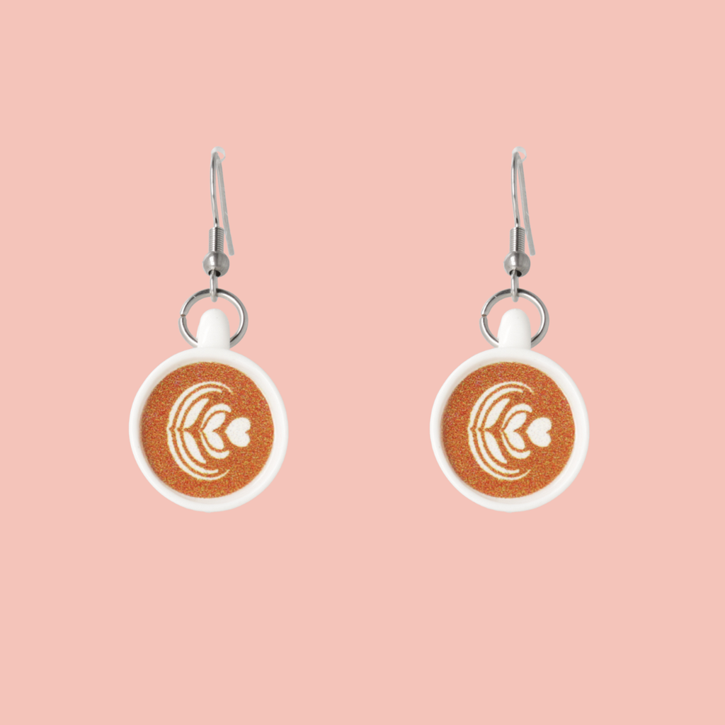 Pair of earrings with coffee cup charm on a pink background