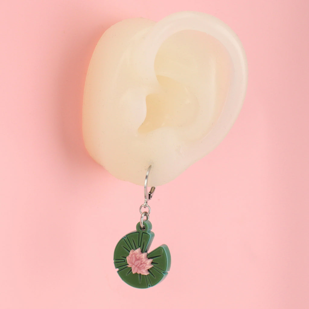 Ear wearing Green acrylic lily pad charms with a pink lotus flower in the centre on stainless steel huggie hoops