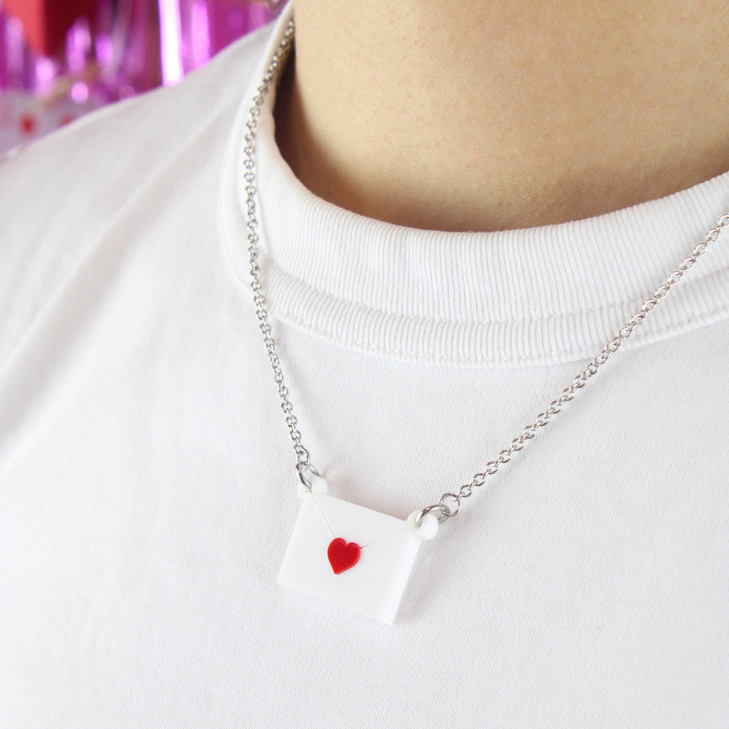 Close up of model wearing love letter pendant featuring a white envelope sealed with a red heart on a stainless steel chain.