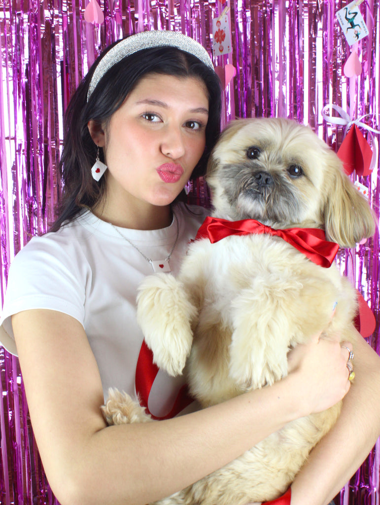 model wearing love letter pendant featuring a white envelope sealed with a red heart on a stainless steel chain. Model is also wearing matching earrings and holding a dog. The dog is wearing a red bow