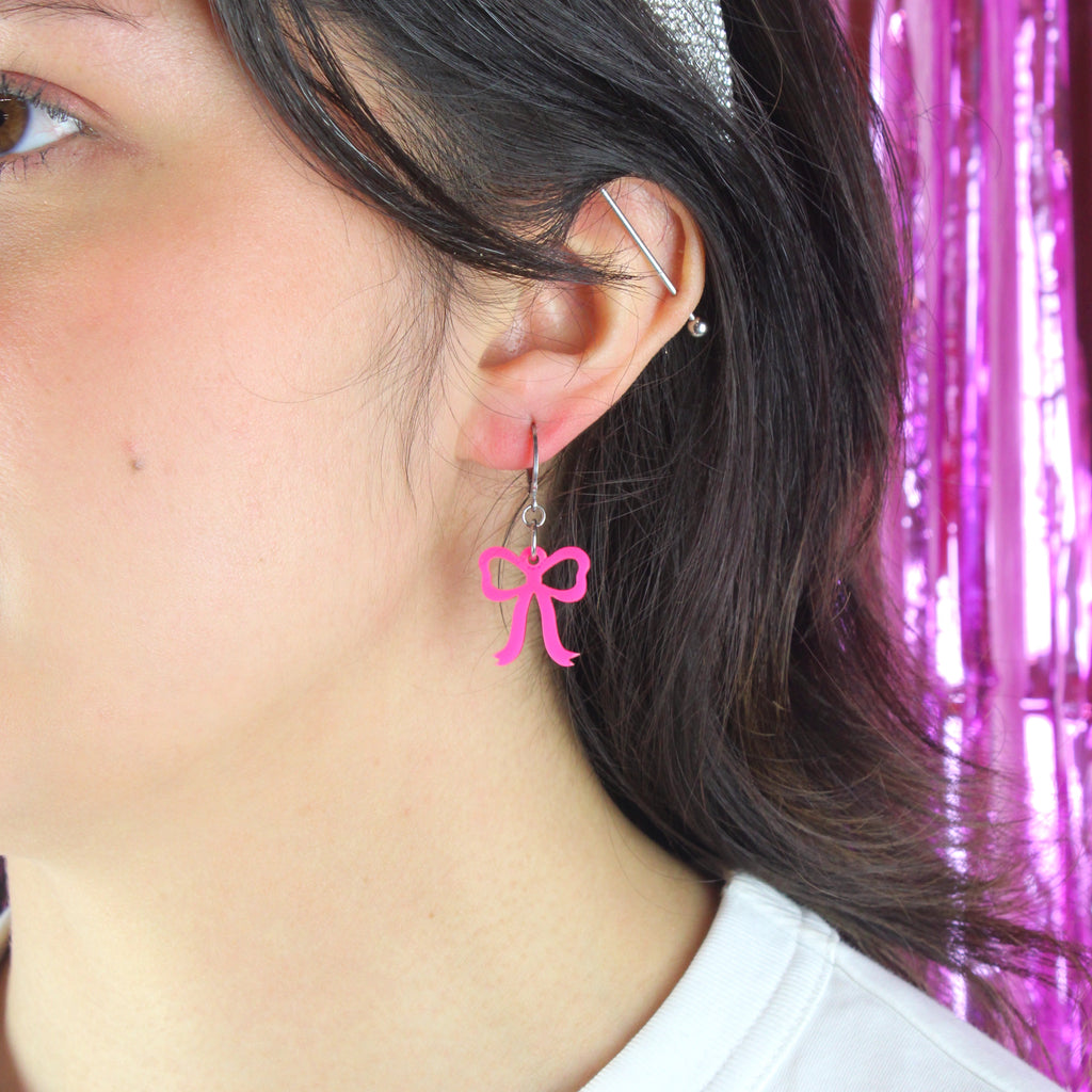Model wearing Bright pink mini bow charms on stainless steel huggie hoops