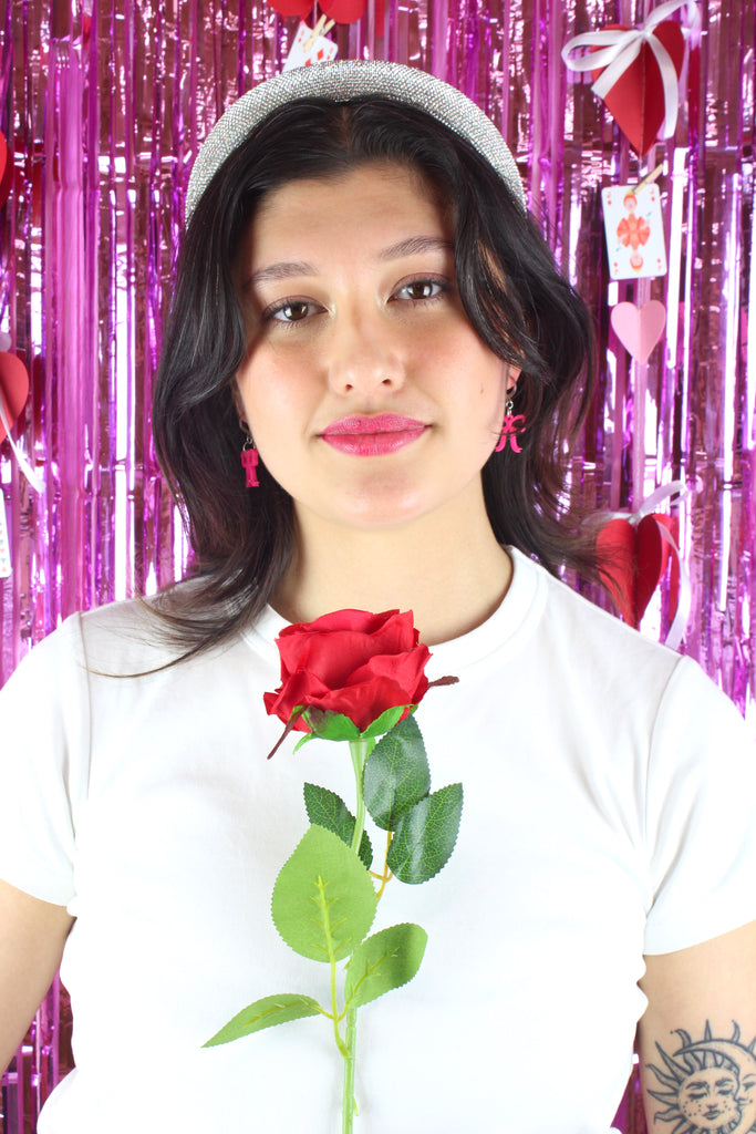 Bright pink mini bow charms on stainless steel huggie hoops, Model is also holding a red rose.