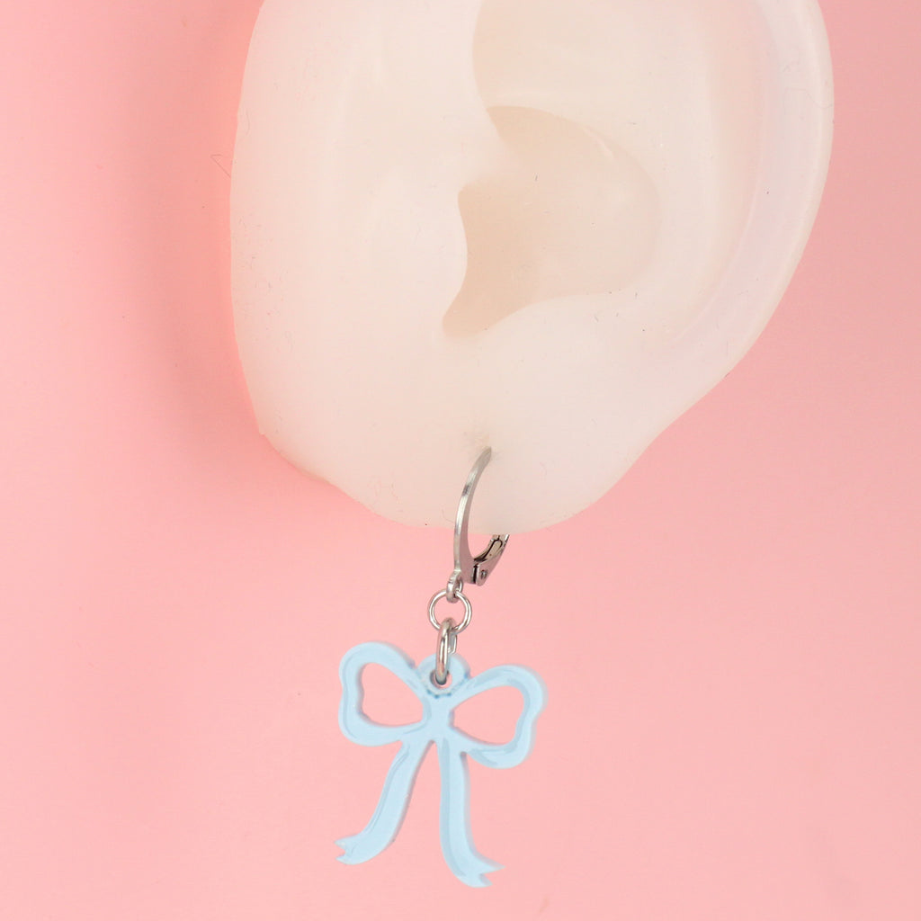 Ear wearing Baby blue bow charms on stainless steel huggie hoops