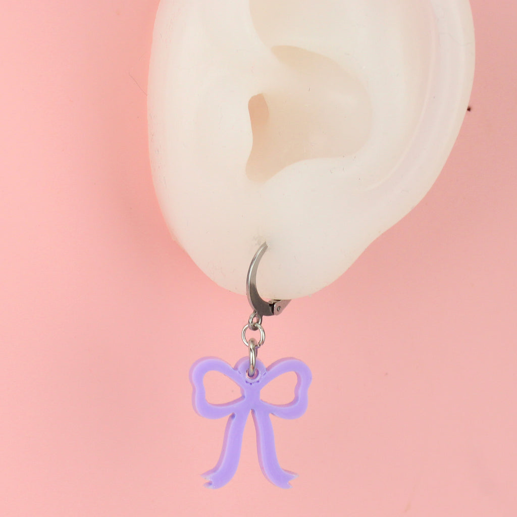 Ear wearing Lilac coloured bow charms on stainless steel huggie hoops