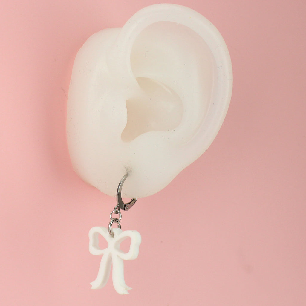 Ear wearing white bow charms on stainless steel huggie hoops