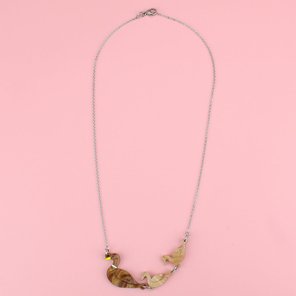 A brown acrylic mother duck pendant with two light brown marble duckling pendants following behind, on a stainless steel chain