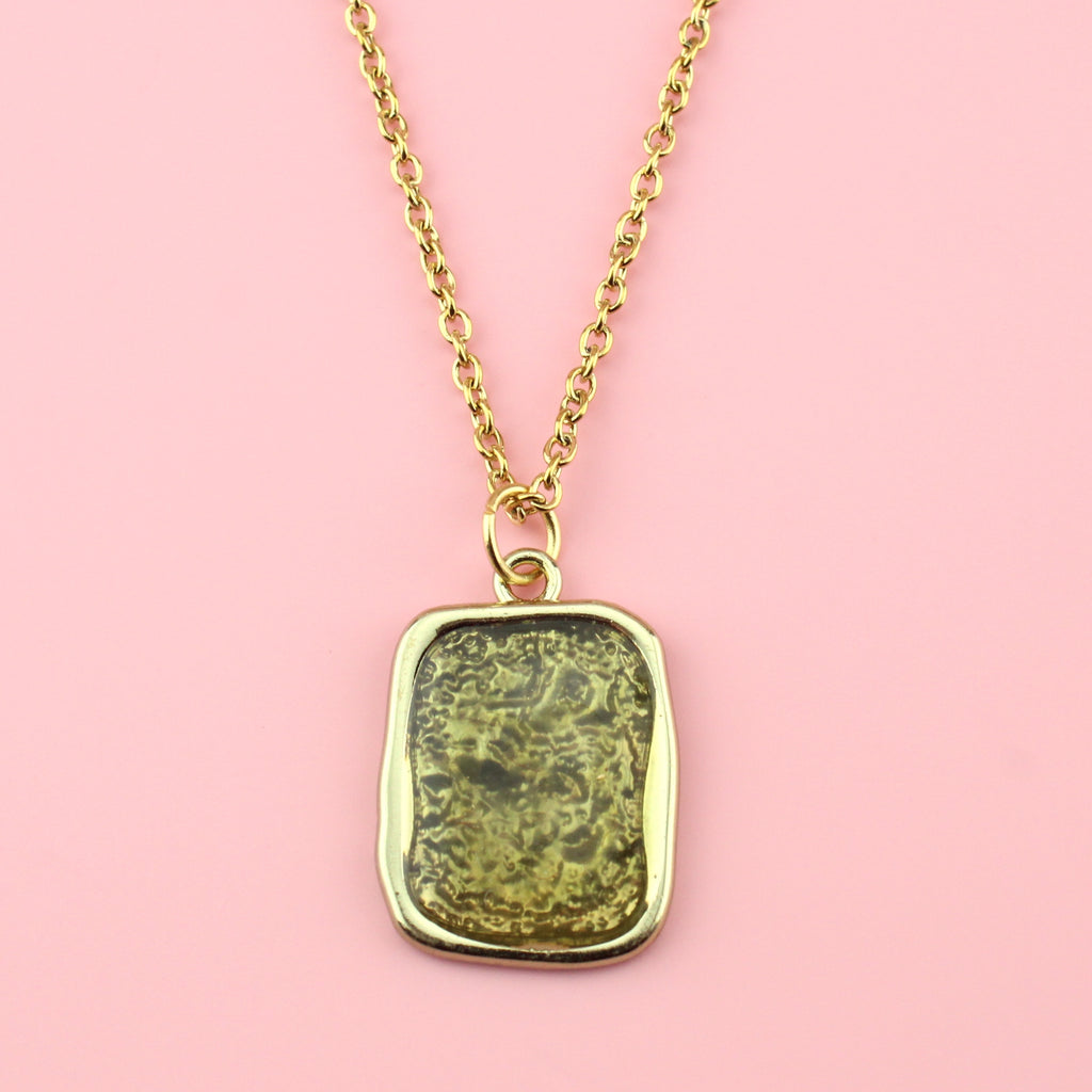 Gold rectangular shaped pendant with a wavy outline and a shimmery olive coloured centre on a gold plated stainless steel chain