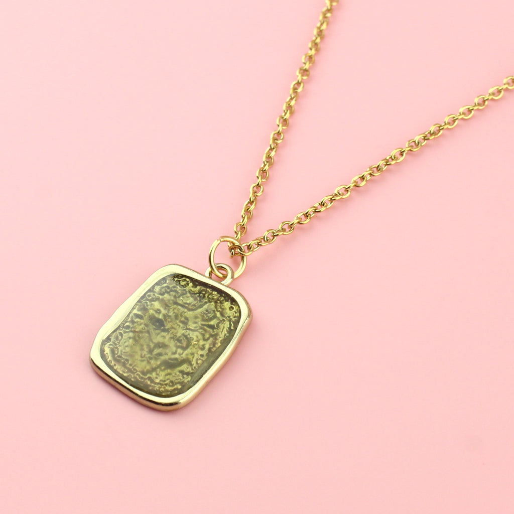 Gold rectangular shaped pendant with a wavy outline and a shimmery olive coloured centre on a gold plated stainless steel chain