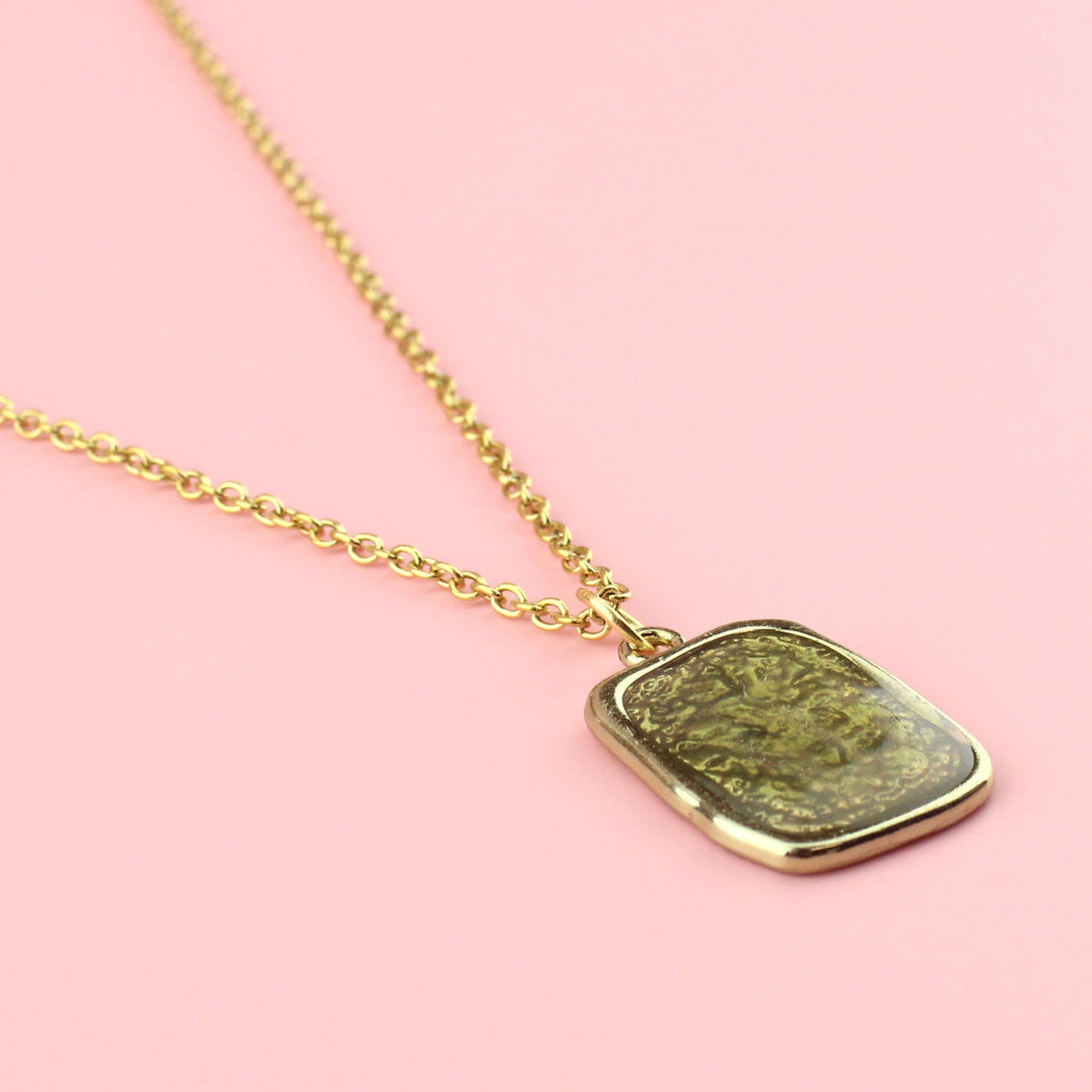 Gold rectangular shaped pendant with a wavy outline and a shimmery olive coloured centre on a gold plated stainless steel chain