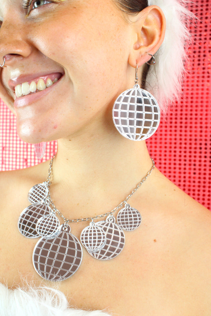 Model wearing Necklace with disco ball pendants varying in size. there are four small disco balls, 2 medium sized disco balls and a large disco ball at the bottom. Model is also wearing the matching earrings