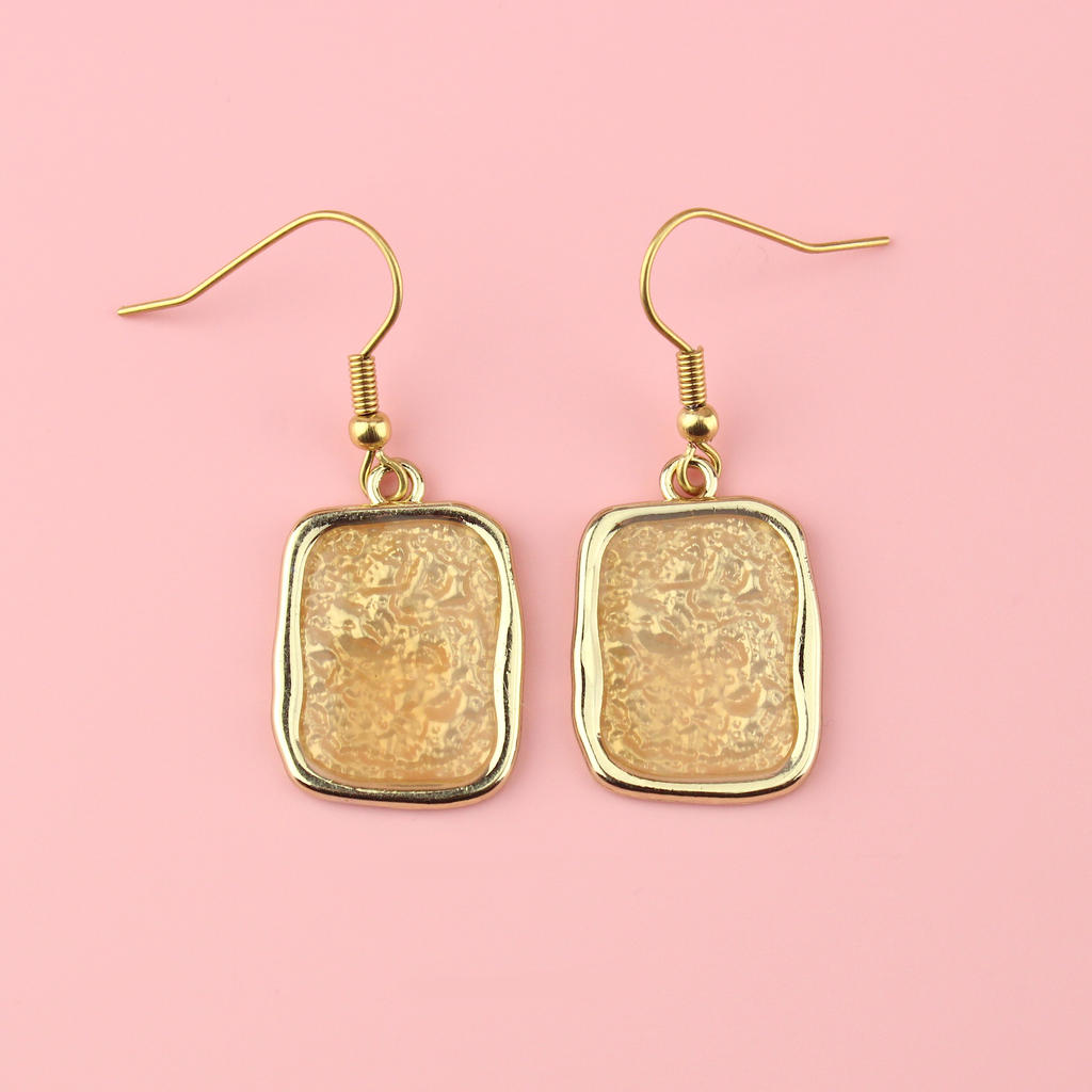 Gold rectangular shaped earrings with a wavy outline and a shimmery peach coloured centre