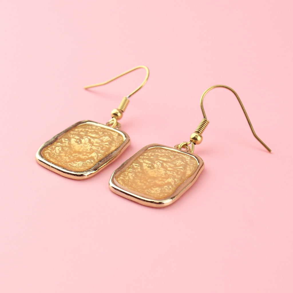 Gold rectangular shaped earrings with a wavy outline and a shimmery peach coloured centre