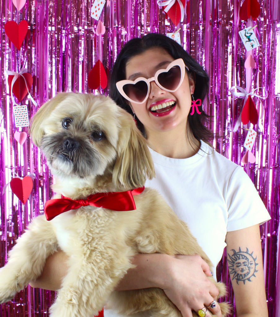 Model wearing Hot Pink Bow Charms on stainless steel earwires holding a dog with a red bow tie