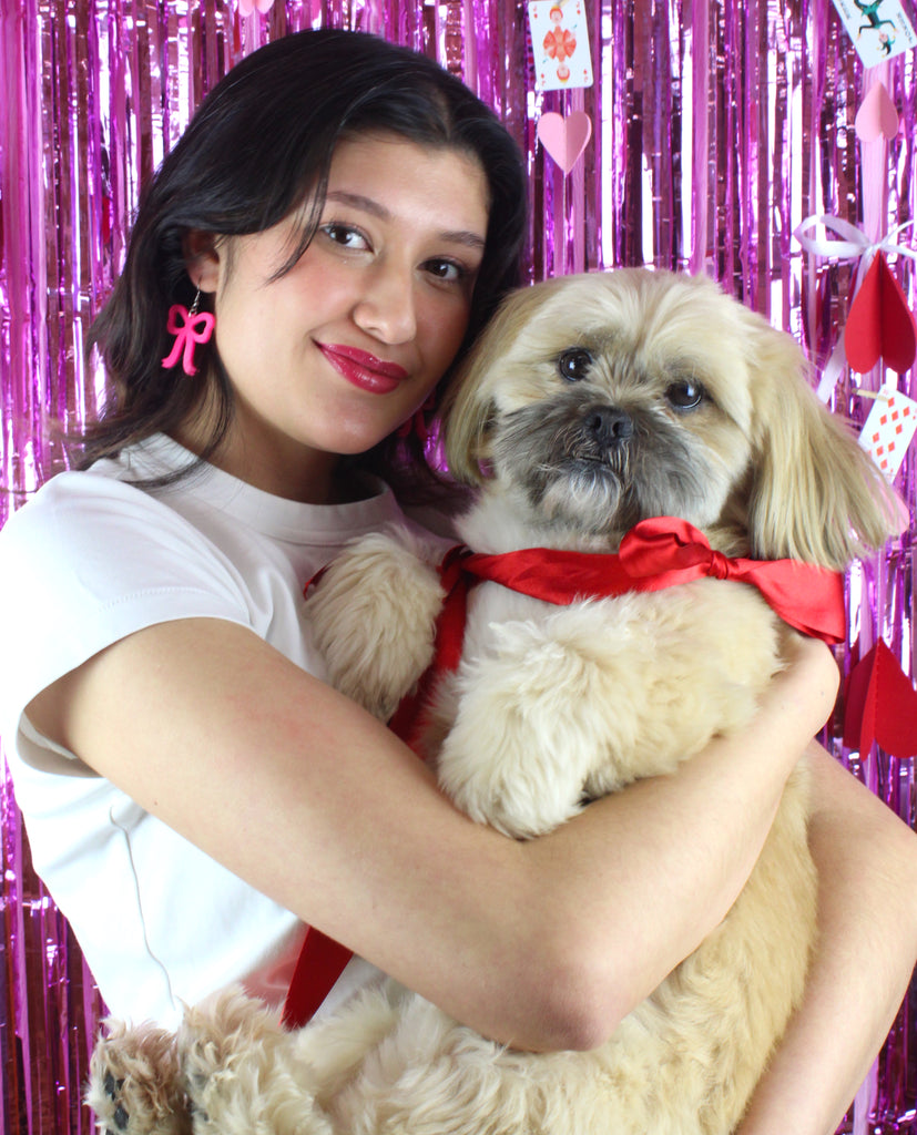 Model wearing Hot Pink Bow Charms on stainless steel earwires holding a dog with a red bow tie