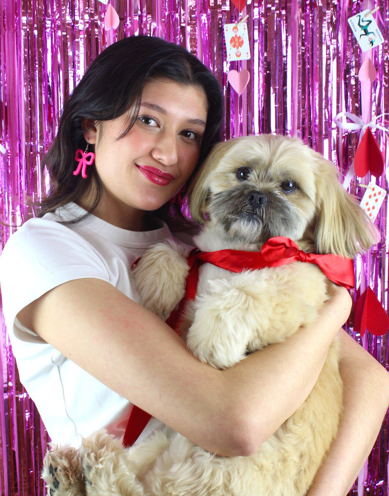 Model wearing Hot Pink Bow Charms on stainless steel earwires holding a dog with a red bow tie