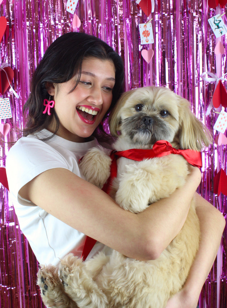 Model wearing Hot Pink Bow Charms on stainless steel earwires holding a dog with a red bow tie