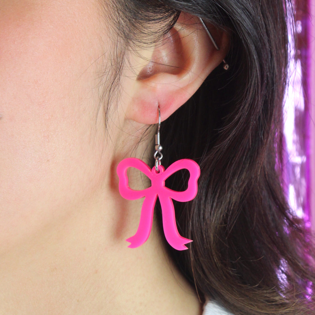 Model wearing Hot Pink Bow Charms on stainless steel earwires holding a dog with a red bow tie