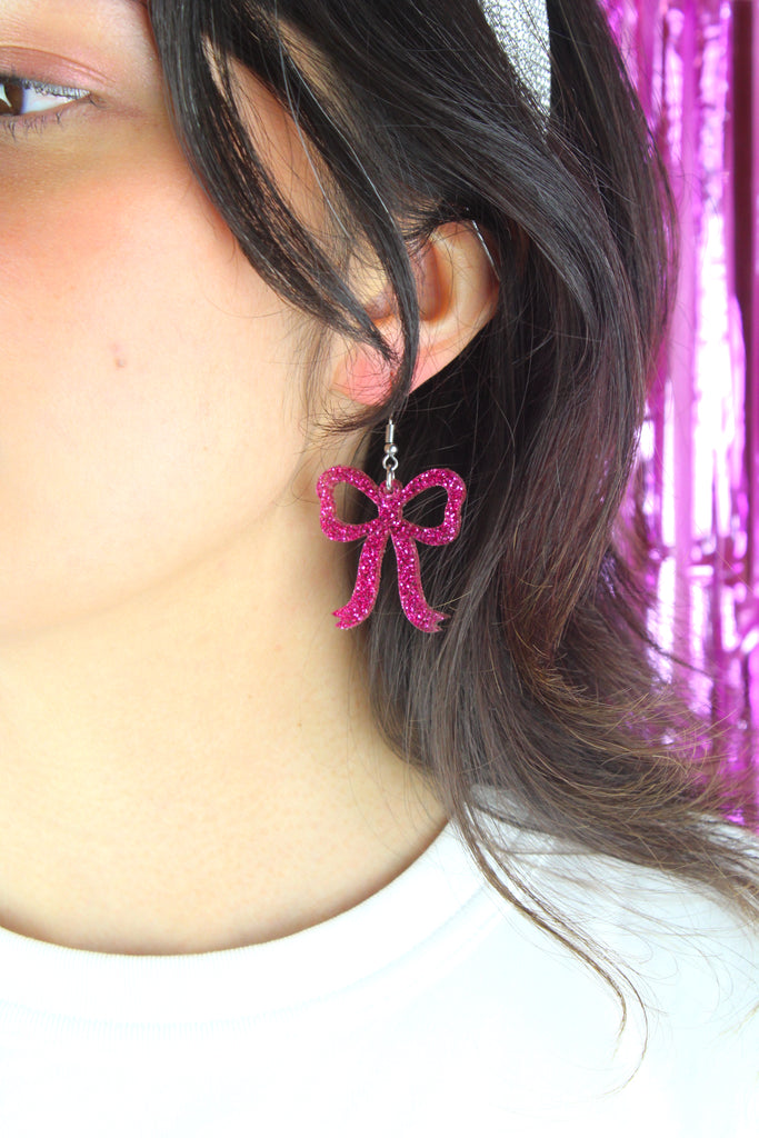 Model wearing Pink glitter bow charms on stainless steel earwires