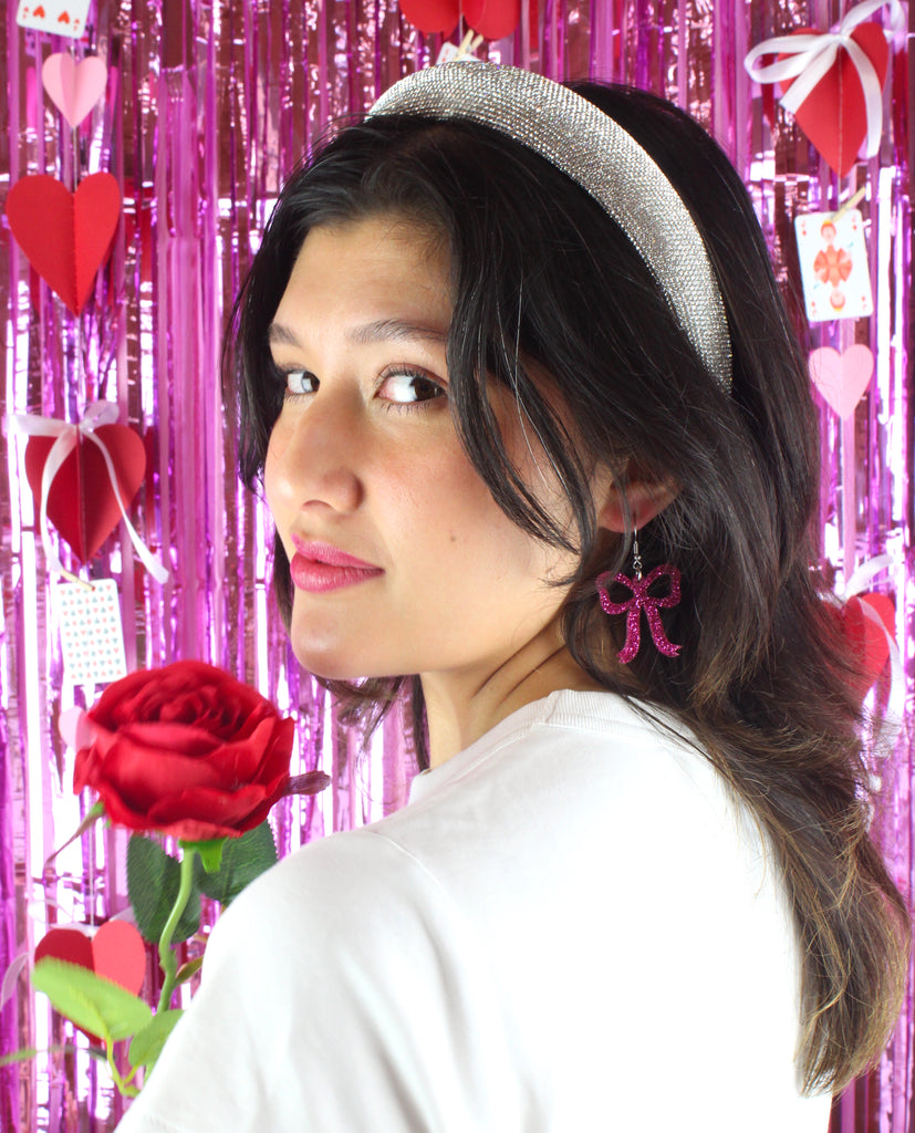 Model wearing Pink glitter bow charms on stainless steel earwires.  Model is also holding a red rose.
