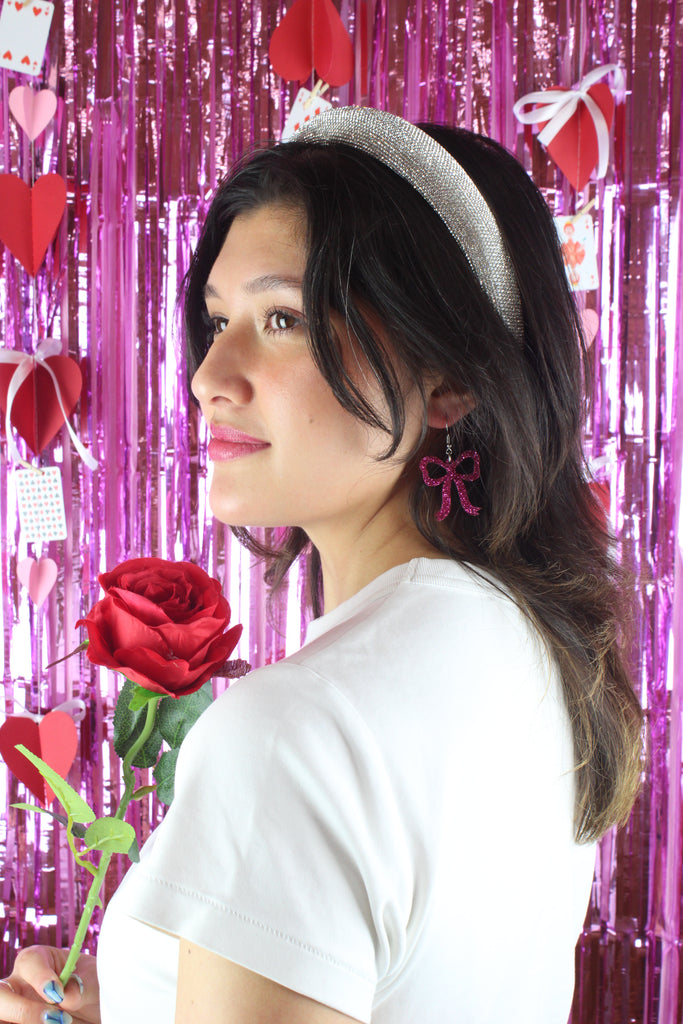 Model wearing Pink glitter bow charms on stainless steel earwires.  Model is also holding a red rose.