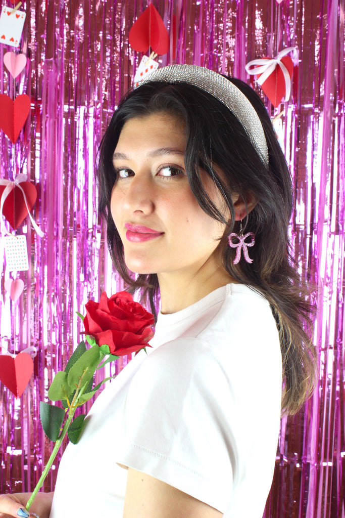Model wearing Pink glitter bow charms on stainless steel earwires. Model is also holding a red rose.
