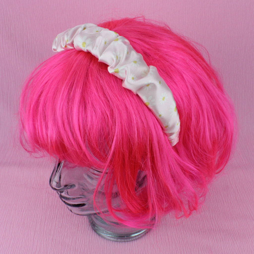 Pastel pink scrunchie style headband with a daisy design shown on a wig for scale