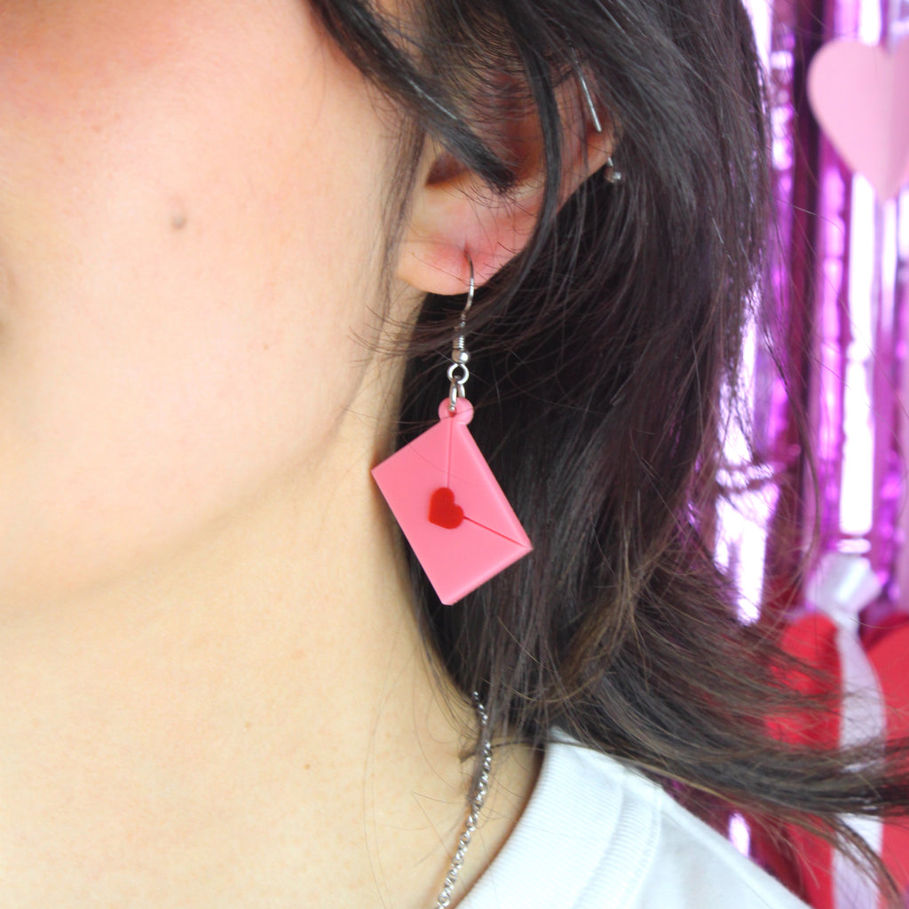 Model wearing acrylic pink envelopes, each sealed with a red heart, and attached to stainless steel earwires