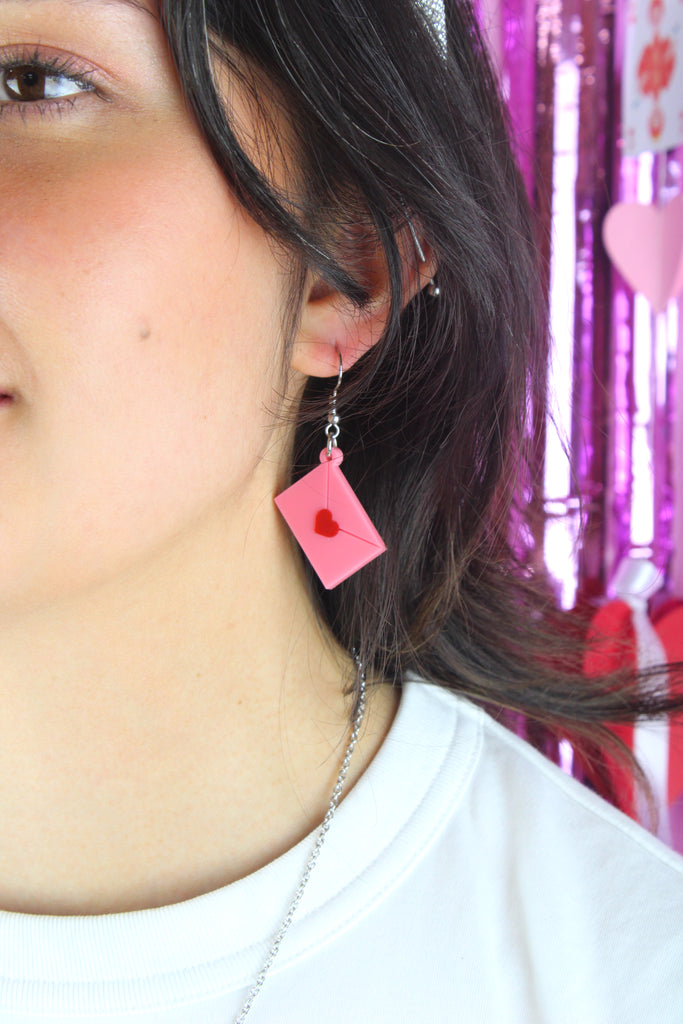 Model wearing acrylic pink envelopes, each sealed with a red heart, and attached to stainless steel earwires