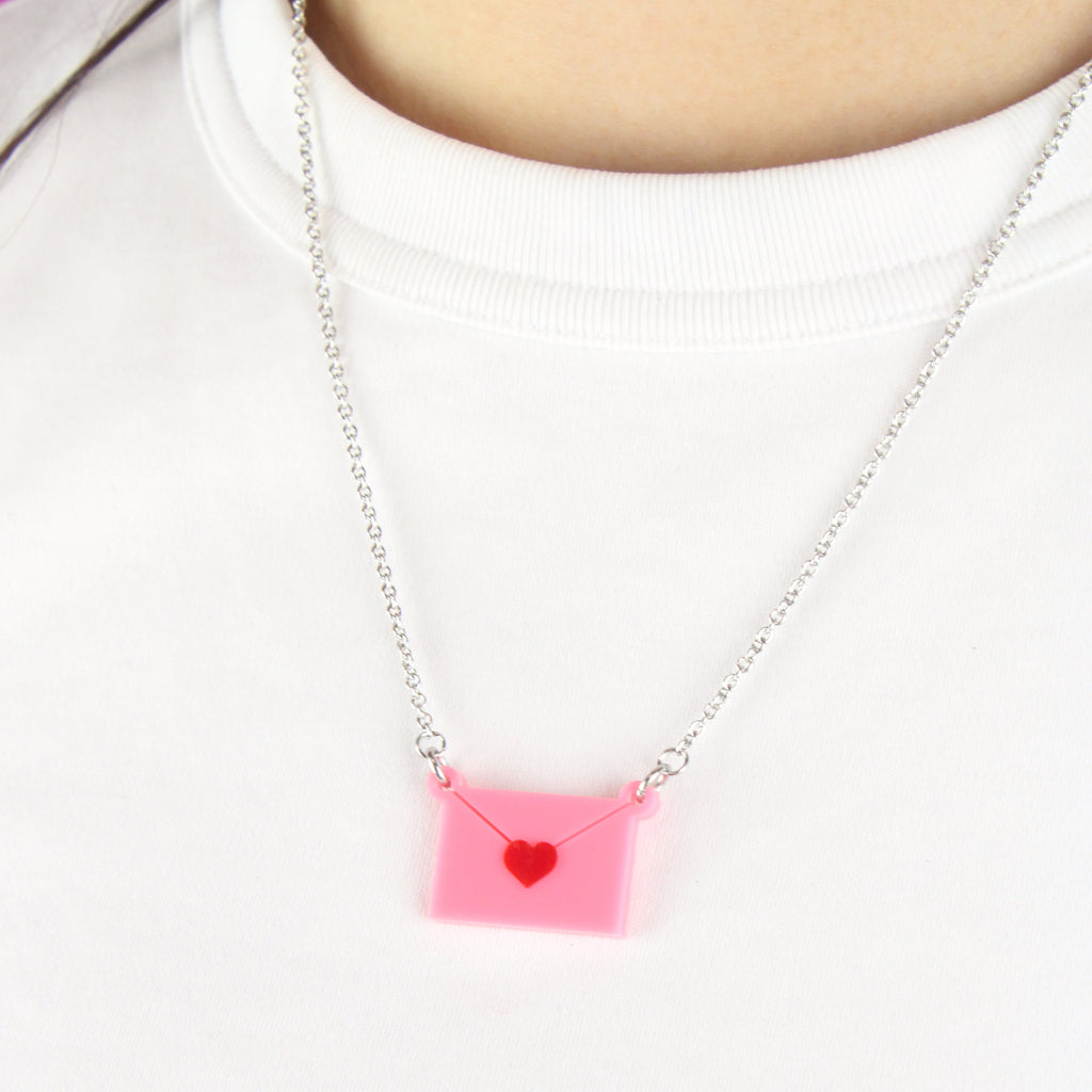 Close up of model wearing pink envelope pendant sealed with a red heart on a stainless steel chain.