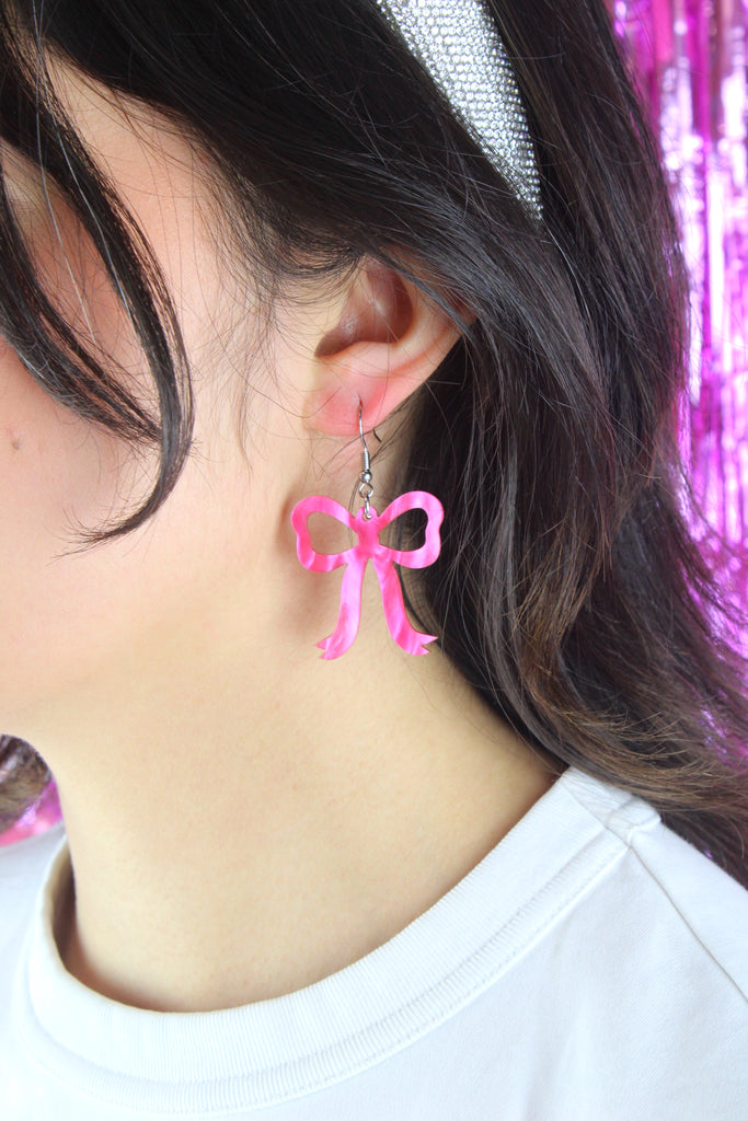 Model wearing Pink marble bow shaped charms on stainless steel earwires