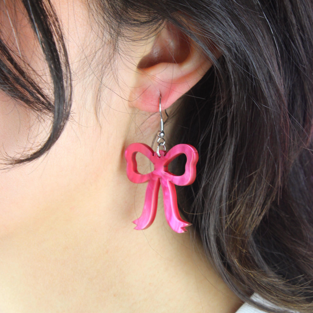 Model wearing Pink marble bow shaped charms on stainless steel earwires