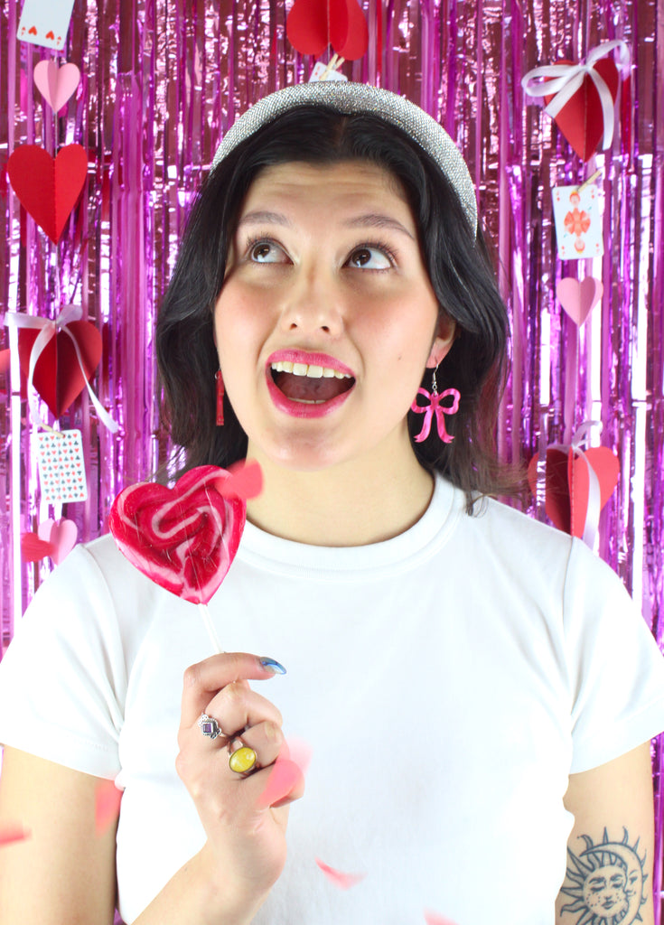 Model wearing Pink marble bow shaped charms on stainless steel earwires. Model is holding a heart-shaped lollipop