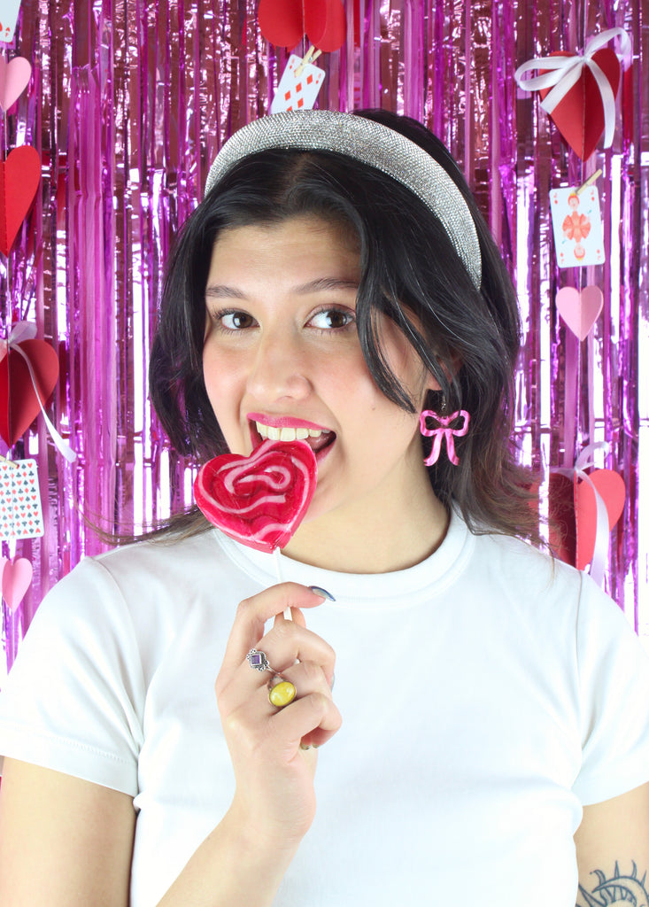 Model wearing Pink marble bow shaped charms on stainless steel earwires and biting on a heart shaped lollipop