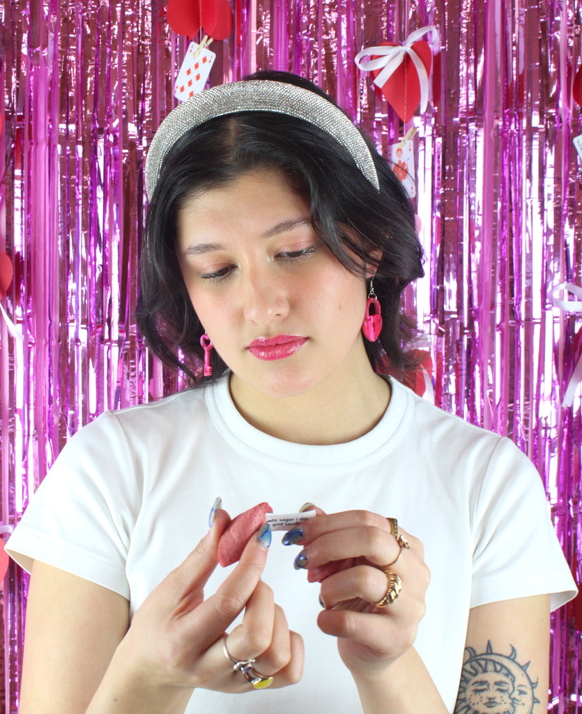 Model wearing pink marble heart padlock and key charms on stainless steel earwires. Model is holding a fortune cookie and reading her fortune.