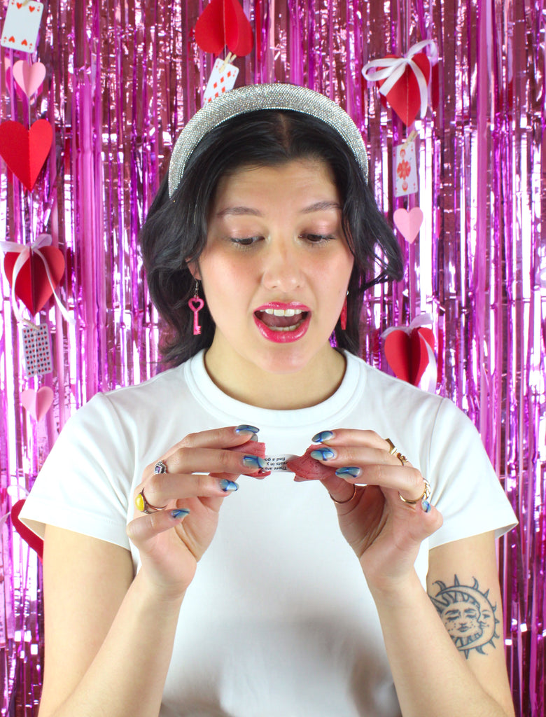 Model wearing pink marble heart padlock and key charms on stainless steel earwires. Model is holding a fortune cookie and reading her fortune.