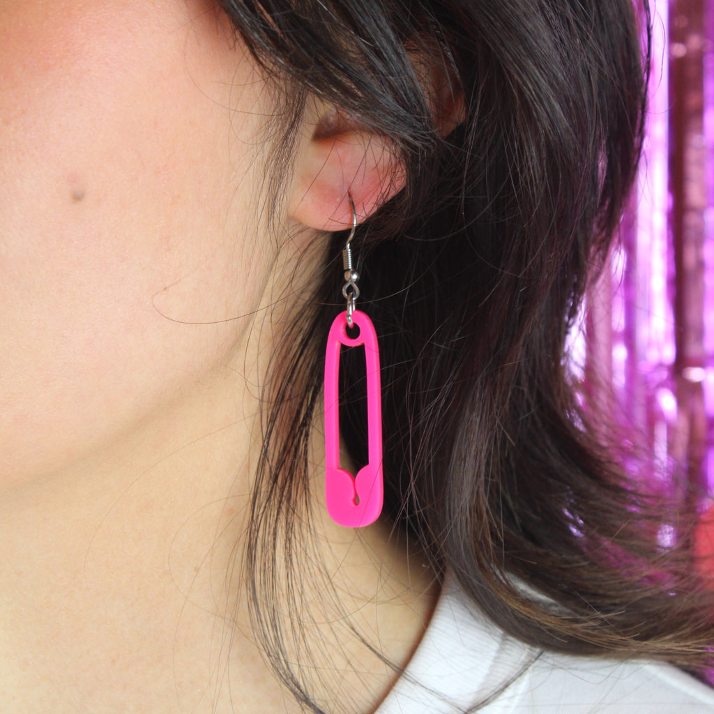 Model wearing Neon pink acrylic charms in the shape of a safety pin on stainless steel earwires