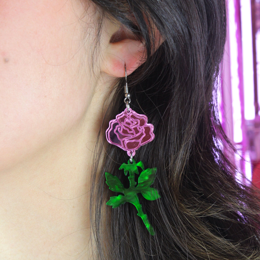 model wearing pink mirror acrylic roses and charming green acrylic thorn charms joined together hanging from stainless steel earwires