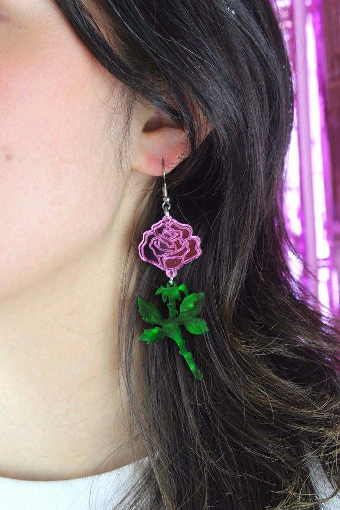 model wearing pink mirror acrylic roses and charming green acrylic thorn charms joined together hanging from stainless steel earwires