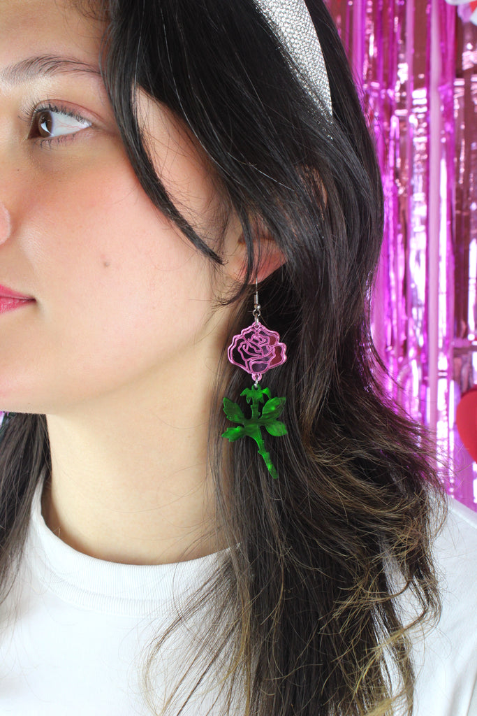 model wearing pink mirror acrylic roses and charming green acrylic thorn charms joined together hanging from stainless steel earwires