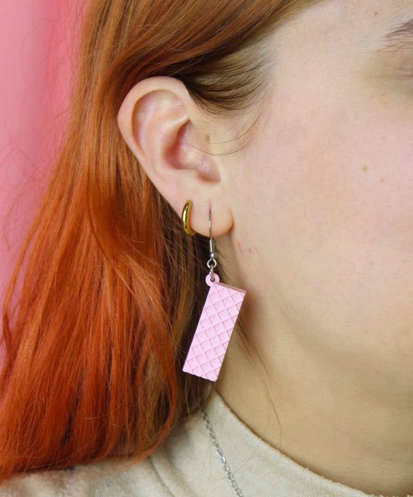 Close-up of a person wearing pink wafer earrings with a pink background