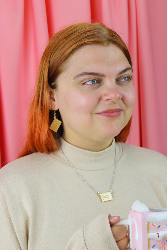 Woman with red hair holding a pink mug against a pink curtain background