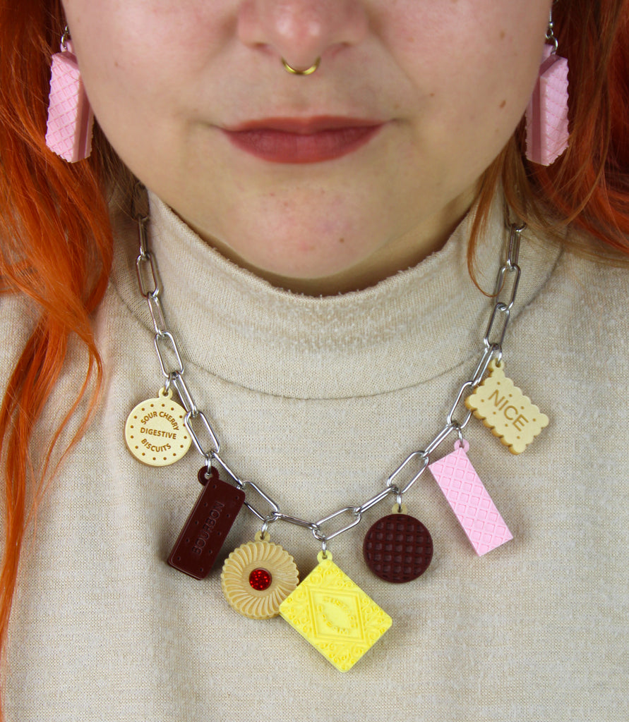 Necklace with cookie-shaped charms worn by a person with red hair and pink earrings.