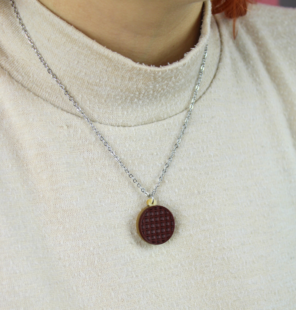 Necklace with a chocolate digestive pendant worn by a person on a light beige background