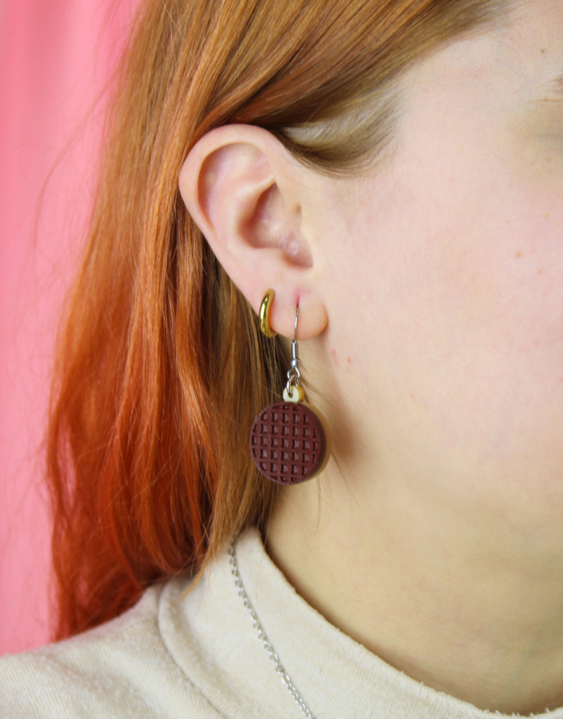 Close-up of a person wearing chocolate digestive earrings with a pink background