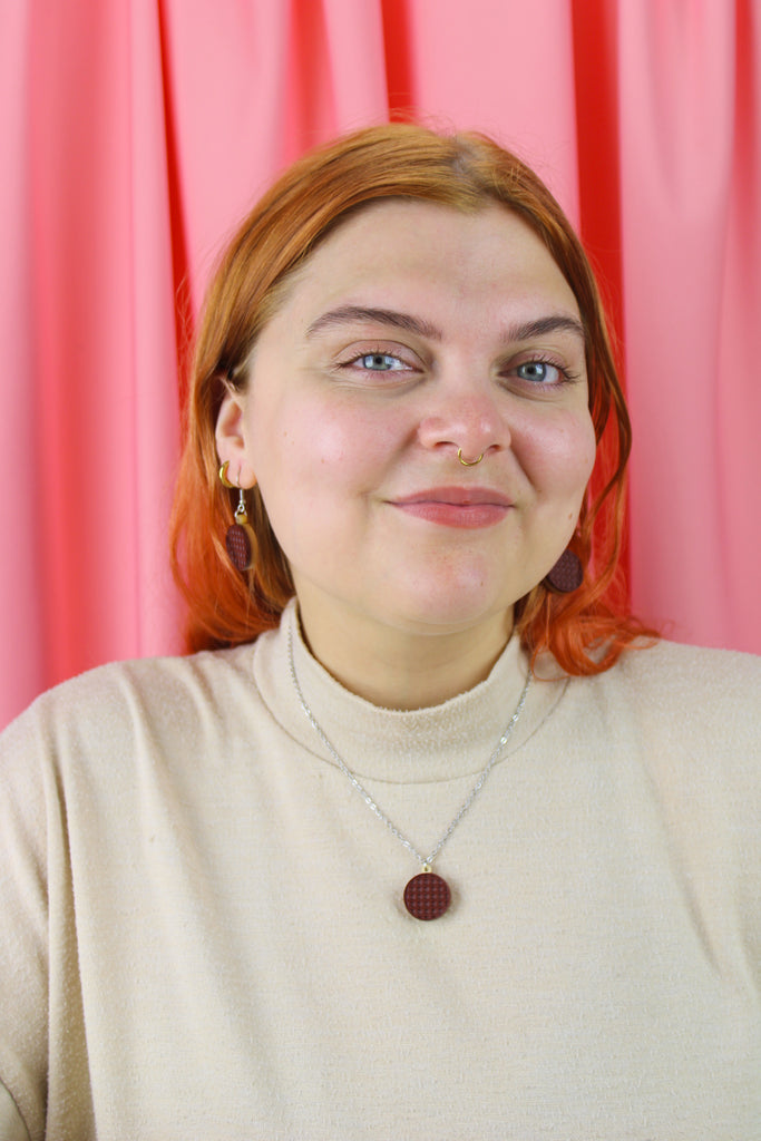 Person with red hair wearing a beige sweater against a pink curtain background