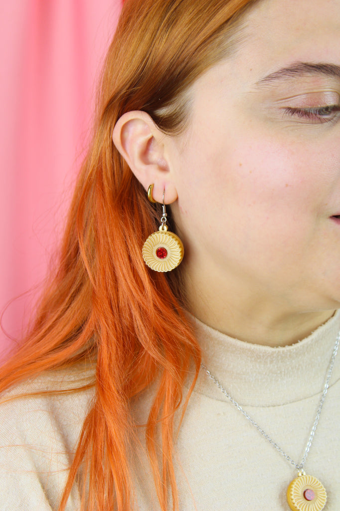 Model wearing a pair of earrings with jam and cream biscuit charms 