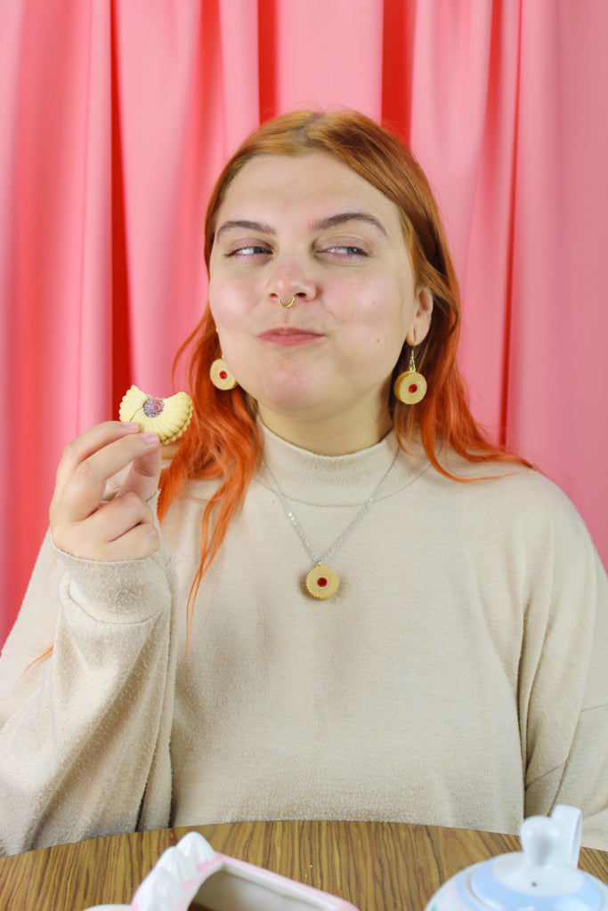 Person with red hair holding a cookie in front of a pink curtain