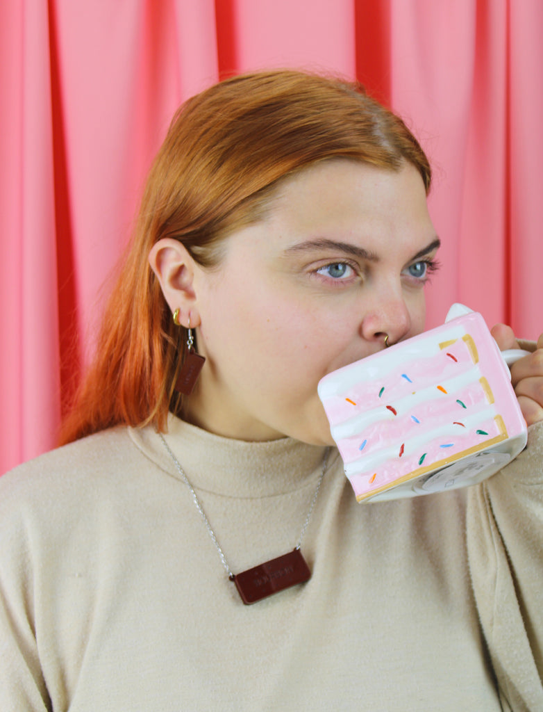 Person holding a mug with a colorful design against a pink curtain background