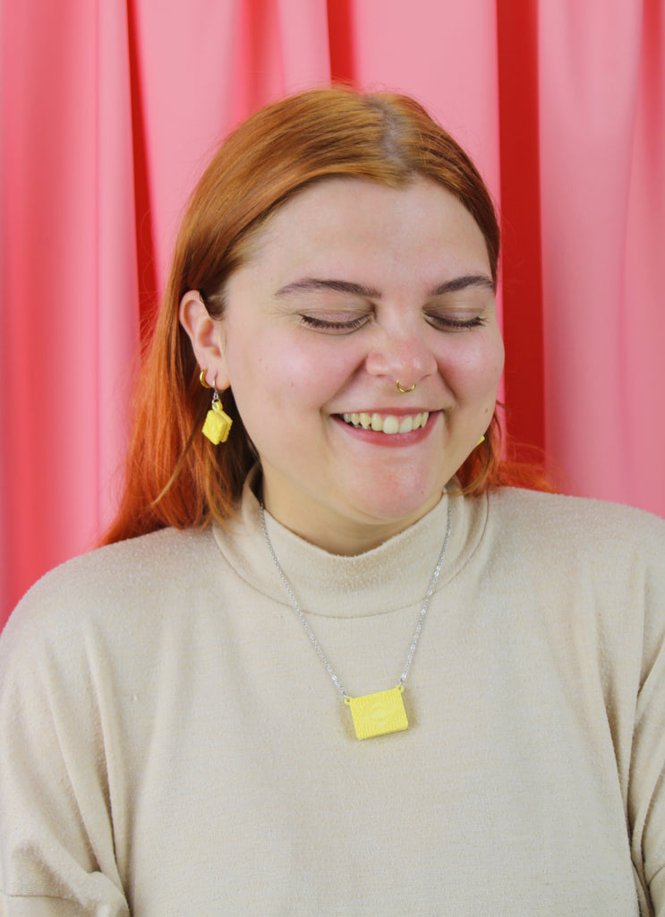 Person with red hair and a beige sweater against a pink curtain background