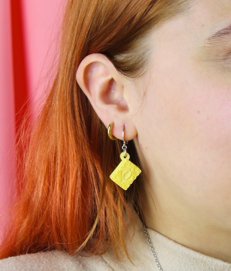 Close-up of a person wearing custard cream earrings with a pink background